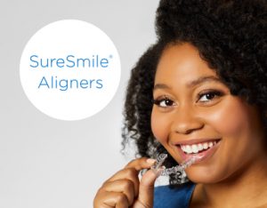 Black woman smiling at camera holding clear aligner with SureSmile logo