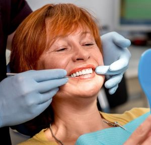 Older woman smiling into mirror as dentist shows her teeth