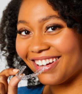 Black woman holding invisible, clear aligner and smiling